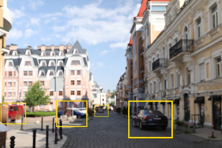 Immagine di una strada cittadina popolata di auto, di cui alcune identificabili e altre meno, evidenziate all’interno di riquadri gialli, a esprimere il concetto di visione artificiale per la robotica.